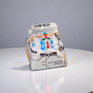 Peut inclure: Un objet rectangulaire en r&eacute;sine transparente avec un design d&eacute;taill&eacute;. L'objet pr&eacute;sente un int&eacute;rieur color&eacute; avec des accents bleus, rouges et dor&eacute;s. Le texte "BREAKWOODEN 2022" est visible sur le c&ocirc;t&eacute;.