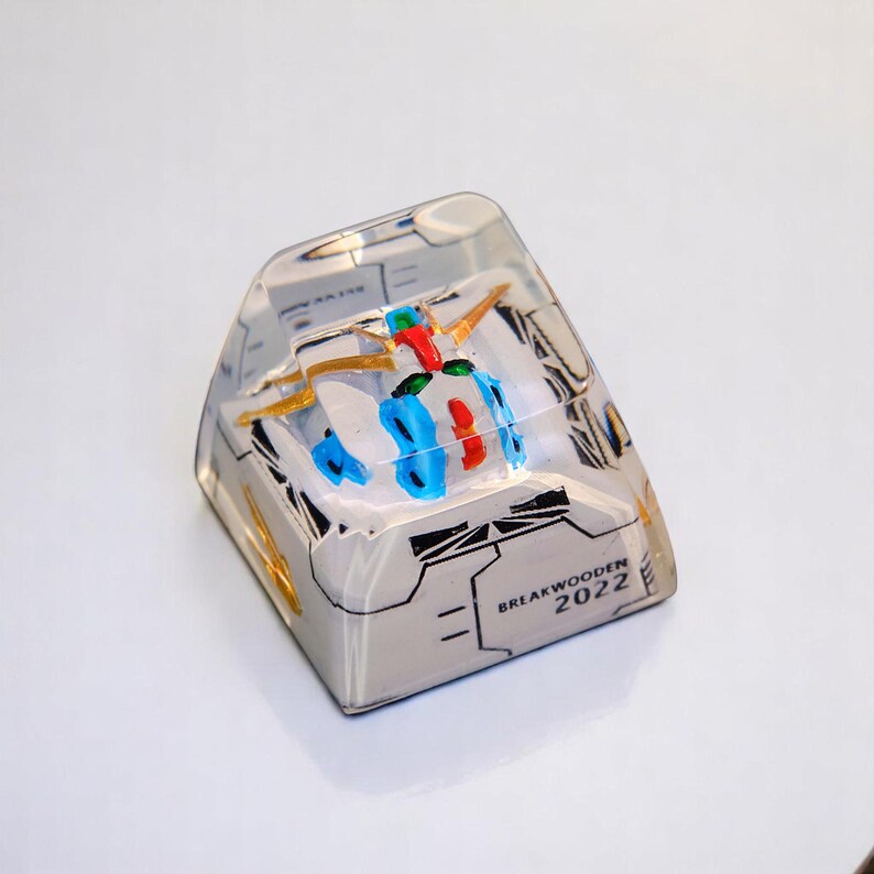 Peut inclure: Un keycap en r&eacute;sine transparente avec un design abstrait color&eacute;. Le design comprend des accents rouges, bleus et dor&eacute;s. Le keycap porte le texte "BREAKWOODEN 2022" sur le c&ocirc;t&eacute;.