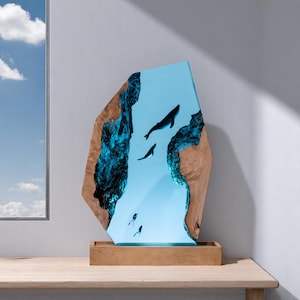 May include: A wooden sculpture with a blue resin inlay depicting whales and scuba divers. The sculpture is on a wooden base.