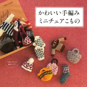 May include: A collection of miniature crochet items including sweaters, hats, socks, and bags in various colors and patterns. Some items are inside a wooden box. The image features Japanese text that reads "かわいい手編みミニチュアこもの" and "気軽にどんどん編めちゃう!".