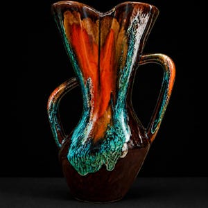 Könnte beinhalten: Eine Keramikvase mit einer einzigartigen Form und zwei Griffen. Die Vase hat eine auffällige Farbpalette aus Braun, Orange, Türkis und Weiß mit glänzendem Finish. Das Design ist abstrakt, wobei die Farben ineinander übergehen und an den Seiten heruntertropfen. Es ist ein dekorativer Artikel.