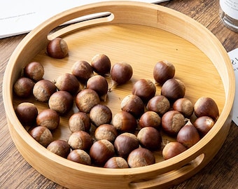May include: A round wooden tray with two handles on the sides. The tray is filled with brown chestnuts.