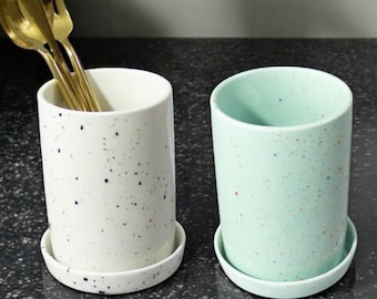 May include: Two ceramic utensil holders with speckled patterns. One is white with black speckles and the other is light green with multi-colored speckles.