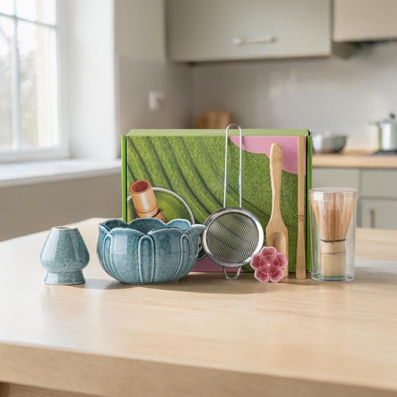 May include: A matcha tea set with a blue ceramic bowl, whisk, scoop, and sifter. The set includes a bamboo whisk, a small ceramic cup, and a decorative pink flower. The box has a green leaf design.