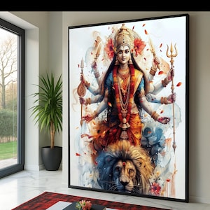 Puede incluir: Una impresión en acuarela enmarcada de una deidad de múltiples brazos, adornada con una corona y joyas doradas, sosteniendo varias armas. La deidad está representada en colores vibrantes, con un sari naranja y azul, y está sentada sobre un león. La obra de arte está sobre un fondo blanco.