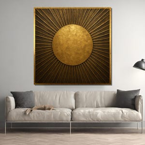 May include: A large, square wall art piece with a gold sunburst design. The central sun is a textured gold circle, surrounded by radiating lines in a darker gold hue. The artwork is framed in a gold border, creating a striking visual statement.