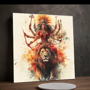 May include: A square canvas print featuring a vibrant watercolor illustration of a multi-armed deity riding a lion. The deity is adorned in red and gold, holding various weapons. The lion is depicted with a detailed mane, set against a backdrop of orange and yellow hues.