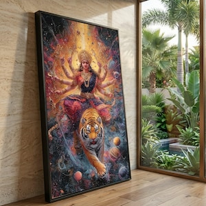 Op de afbeelding: Een ingelijst kunstwerk toont een veelarmige godheid die op een tijger rijdt, tegen een kosmische achtergrond. Het kunstwerk heeft levendige kleuren, waarbij de godheid is versierd met sierlijke sieraden en een kroon. De tijger is oranje en zwart, en het kunstwerk is zwart omlijst.