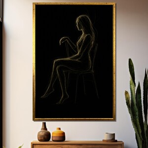 May include: A framed artwork featuring a gold-toned sketch of a person seated in a chair against a black background. The artwork is in a gold frame and is displayed on a wall above a wooden cabinet. Decorative vases and a plant are also visible.