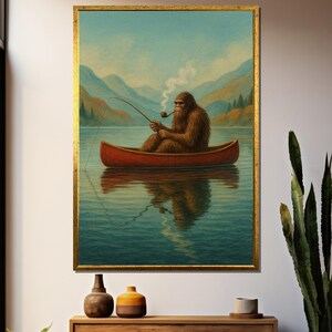 Puede incluir: Una impresión artística enmarcada representa a un Sasquatch en una canoa roja, pescando en un lago. La criatura, con pelaje marrón, fuma una pipa. Montañas y un cielo azul forman el telón de fondo. La obra de arte está en un marco dorado.