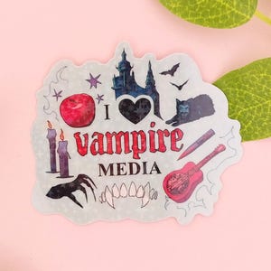 Könnte beinhalten: Ein gestanzter Aufkleber mit dem Text I love vampire MEDIA in Rot und Schwarz. Die Illustrationen zeigen einen roten Apfel, ein dunkles Schloss, eine schwarze Katze, zwei violette Kerzen, eine Klauenhand, Reißzähne, einen Pflock und eine rote Gitarre.