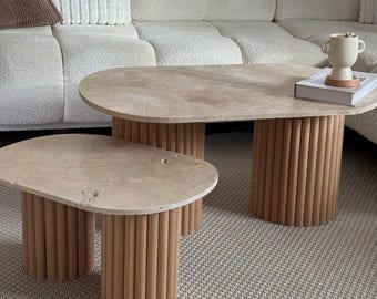 Peut inclure: Deux tables basses ovales avec des plateaux beiges clairs et des bases en baguettes de bois verticales. La plus grande table mesure environ 122 cm de long, et la plus petite, environ 76 cm. Elles sont posées sur un tapis neutre, pour un style moderne.