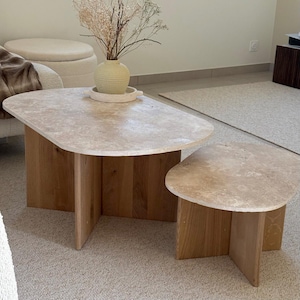 Peut inclure: Un ensemble de tables basses modernes avec un plateau en pierre claire et une base en bois naturel. La table la plus grande mesure environ 122 cm de long et 61 cm de large. L'ensemble comprend une petite table d'appoint.