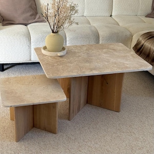 Peut inclure: Ensemble de deux tables basses. Les tables ont un plateau rectangulaire en pierre beige clair et une base en bois brun clair. La plus grande table mesure 91 cm de long et 61 cm de large. La plus petite table mesure 61 cm de long et 61 cm de large.