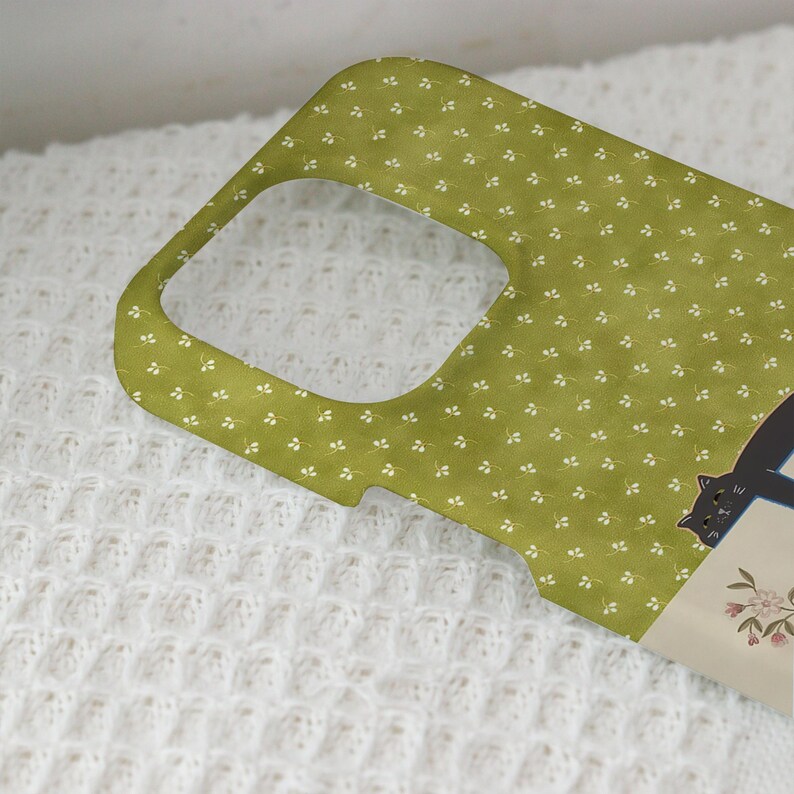 May include: A green phone case with a repeating white floral pattern. A black cat illustration is visible on the side. The case is designed to fit a phone, with cutouts for the camera and buttons.