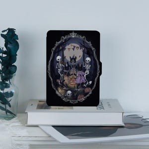 May include: Black tablet case featuring a Halloween-themed illustration. The artwork depicts black cats and skeletons gathered around a bonfire in a forest setting, framed by an ornate oval border. Pumpkins and skulls are also visible.