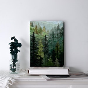 May include: A rectangular art print featuring a watercolor forest scene. The artwork depicts a lush forest with tall evergreen trees in shades of green and brown, with a misty mountain backdrop. The print is displayed on a white surface.
