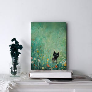 May include: A rectangular notebook featuring a whimsical illustration of a black cat peeking out from a field of wildflowers. The artwork is set against a backdrop of lush green grass and colorful blooms, creating a charming scene.