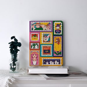 May include: A notebook with a vibrant design of anime characters, presented in stamp-like frames. The cover has a yellow, purple, and green border. The notebook is on a white surface.