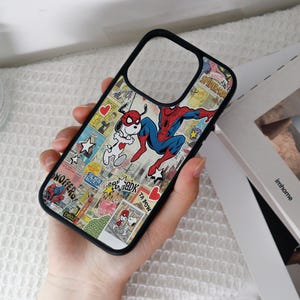 May include: Black phone case featuring a comic book collage design with Spider-Man and Snoopy characters. The case has a black border and a clear cutout for the camera. The background is a mix of comic book panels with various colors and text.