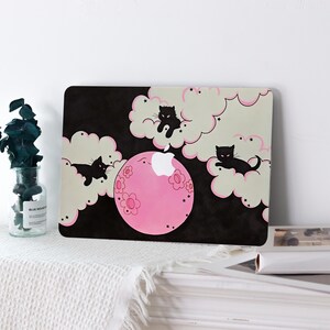 May include: A laptop skin featuring a black background with light-colored clouds outlined in pink. Three black cat silhouettes are positioned within the clouds. A large pink circular moon with flower patterns is centered, incorporating the white Apple logo.