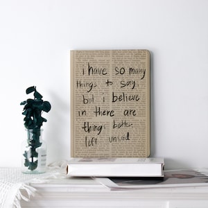 May include: A rectangular wall art print with a vintage newspaper background. The text "I have so many things to say but in there are things better left unsaid" is written in black. A decorative vase with green leaves is on the left.