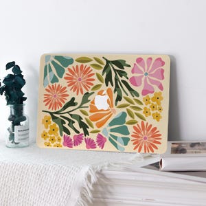 May include: A beige laptop case featuring a colorful floral design. The design includes orange, pink, yellow, and teal flowers with green leaves. The Apple logo is visible in the center of the case.