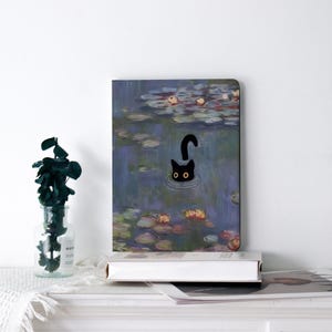 May include: A rectangular art print featuring a black cat swimming in a pond with lily pads. The cat's head and arched back are visible above the water. The artwork is reminiscent of a Monet painting.