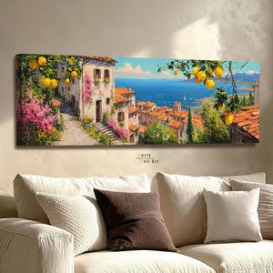 Könnte beinhalten: Ein panoramisches Leinwandbild, das ein mediterranes Küstendorf mit Terrakotta-Dächern, Steinwegen und leuchtend rosa Blumen zeigt. Helle gelbe Zitronen hängen an Zweigen im Vordergrund und blicken auf ein tiefblaues Meer hinaus.
