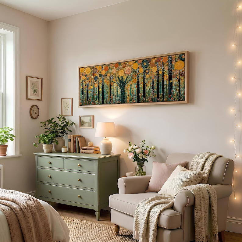 May include: A long rectangular wall art piece featuring a stylized forest with circular golden and orange foliage, framed in light wood. The artwork hangs above a sage green wooden dresser with brass knobs and a white table lamp in a room.