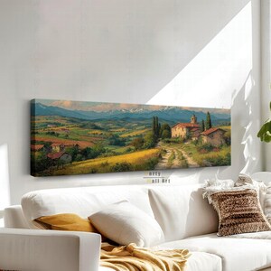 Pode incluir: Uma impressão de arte de parede panorâmica apresentando uma paisagem rural italiana com edifícios de pedra, um caminho de terra, colinas verdes e montanhas distantes com picos nevados sob um céu suave. O texto Morty Wall Art é visível.