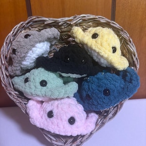 May include: A collection of six small, plush, crocheted stingray toys in various colors including gray, yellow, black, light green, dark blue, and light pink. Each stingray features two black plastic safety eyes and a soft, textured yarn finish.