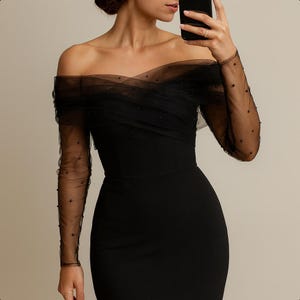 Può includere: Un abito nero con spalle scoperte e maniche trasparenti decorate con piccole perle scure. L'abito presenta un corpetto aderente e una gonna fluida, creando una silhouette elegante. Le maniche sono lunghe e aderenti.