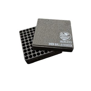 May include: A black square ammunition gauge block with a grid of circular holes. The top surface features a white logo of a stylized bird and the text JACREATES 9MM BALLISTICHECK. The object is shown with a second identical piece underneath.