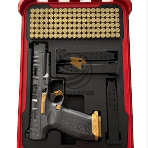 May include: A black handgun with gold accents and a black grip is displayed inside a red case. The case contains ammunition and magazines. The case is open, revealing the contents.