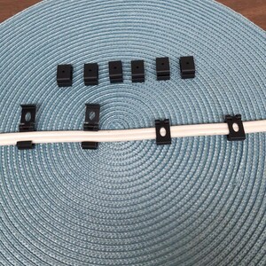 Puede incluir: Clips de cable de plástico negro en una alfombra circular azul con un cable blanco que pasa a través de ellos.