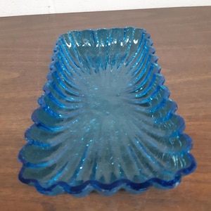 May include: A blue glass serving dish with a scalloped edge. The dish has a rippled texture and is ideal for serving snacks or appetizers.