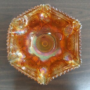 Puede incluir: Un cuenco de vidrio ámbar vintage con un borde festoneado y un patrón decorativo. El cuenco tiene un acabado iridiscente y es perfecto para servir fruta o dulces.