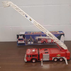 May include: A red toy fire engine with a white ladder extended. The engine has a Sunoco logo on the side and is labelled "Aerial Tower Fire Truck - Marches Edition".
