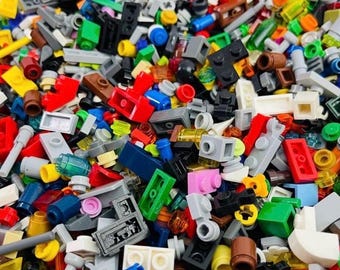 May include: A large collection of assorted plastic building bricks in various shapes, sizes, and colors including red, blue, yellow, green, black, white, gray, and brown. The pile features a mix of standard rectangular blocks, plates, and cylinders.
