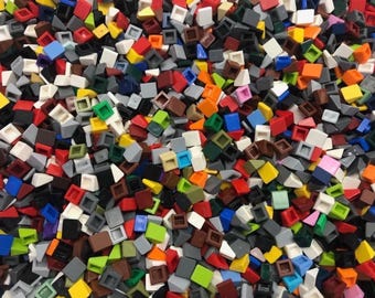 May include: A large collection of small, plastic building block pieces in a variety of colors including red, blue, yellow, green, white, black, gray, brown, and orange. The pieces are shaped as small slopes and squares, scattered together.
