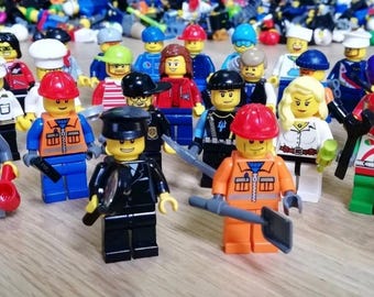 May include: A collection of various plastic minifigures featuring diverse outfits, hats, and accessories. The figures include characters in construction gear, uniforms, and casual clothing, standing together with a large pile of assorted parts behind them.