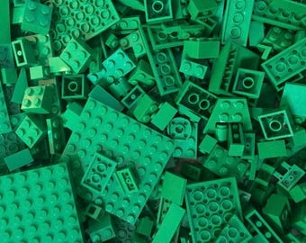May include: A large collection of assorted green plastic building blocks of various shapes and sizes. The pile includes rectangular bricks, square plates, and flat base plates, all featuring the characteristic circular studs on top.