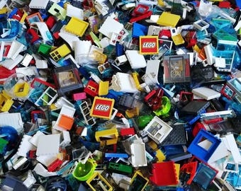 May include: A large, disorganized pile of assorted plastic building blocks and components in various colors, including white, yellow, blue, red, and green. Several pieces feature the red and white LEGO logo, while others include window frames, doors, and transparent panels.