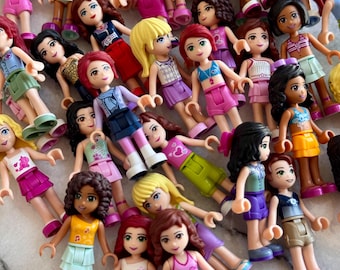 May include: A collection of small plastic dolls with various skin tones, hair colors, and outfits. The dolls are wearing tops and skirts or shorts in shades of pink, purple, blue, and yellow. Some dolls have accessories.