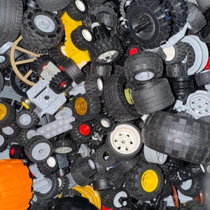 May include: A large collection of black, gray, and white Lego wheels of various sizes and styles. Some wheels have yellow or red accents. The wheels are in a plastic container.