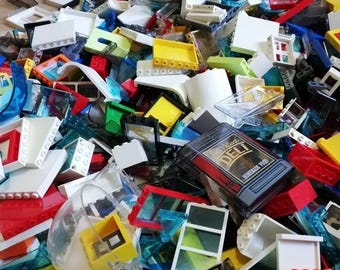 May include: A large collection of assorted plastic building blocks in various colors including white, red, yellow, blue, and green. The pile features numerous translucent pieces, window frames, and a black printed tile labeled Art Village DELI.