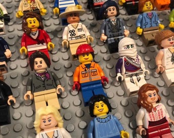 May include: A collection of various plastic minifigures arranged on a gray studded baseplate. The figures feature diverse outfits, including construction gear, formal suits, casual shirts, and ninja attire, with distinct hair colors and facial expressions.