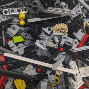 以下が含まれることがあります： グレー、黒、黄色、赤、白など、さまざまな色のプラスチック製のブロックが山積みになっているクローズアップ写真。ブロックはさまざまな形とサイズで、穴、ペグ、その他の接続機能があります。建設玩具。