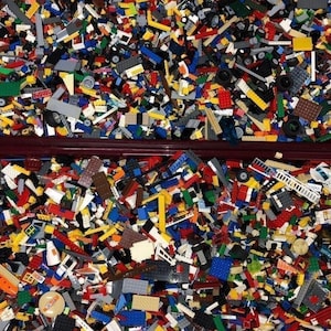 Op de afbeelding: Een grote verzameling kleurrijke plastic bouwstenen, waaronder rode, gele, blauwe en groene stukken, die twee containers vullen. De stenen variëren in grootte en vorm, wat wijst op een verscheidenheid aan bouwmogelijkheden.